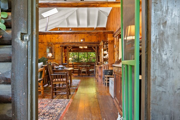 Interior de una cabaña de troncos con comedor, muebles de madera y vistas por una ventana.