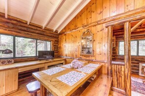 L’intérieur d’un chalet en bois, avec une longue table à manger, un téléviseur et un miroir au mur.