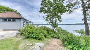 A house with a view of a lake, surrounded by greenery and a clear sky.