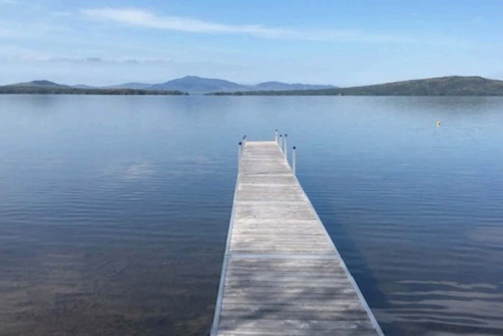 Une jetée en bois s’étendant sur une étendue d’eau calme, avec des montagnes visibles au loin.
