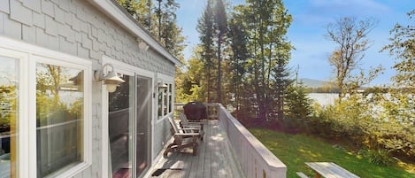 A wooden deck with a covered area, outdoor seating, and a view of trees and a body of water.