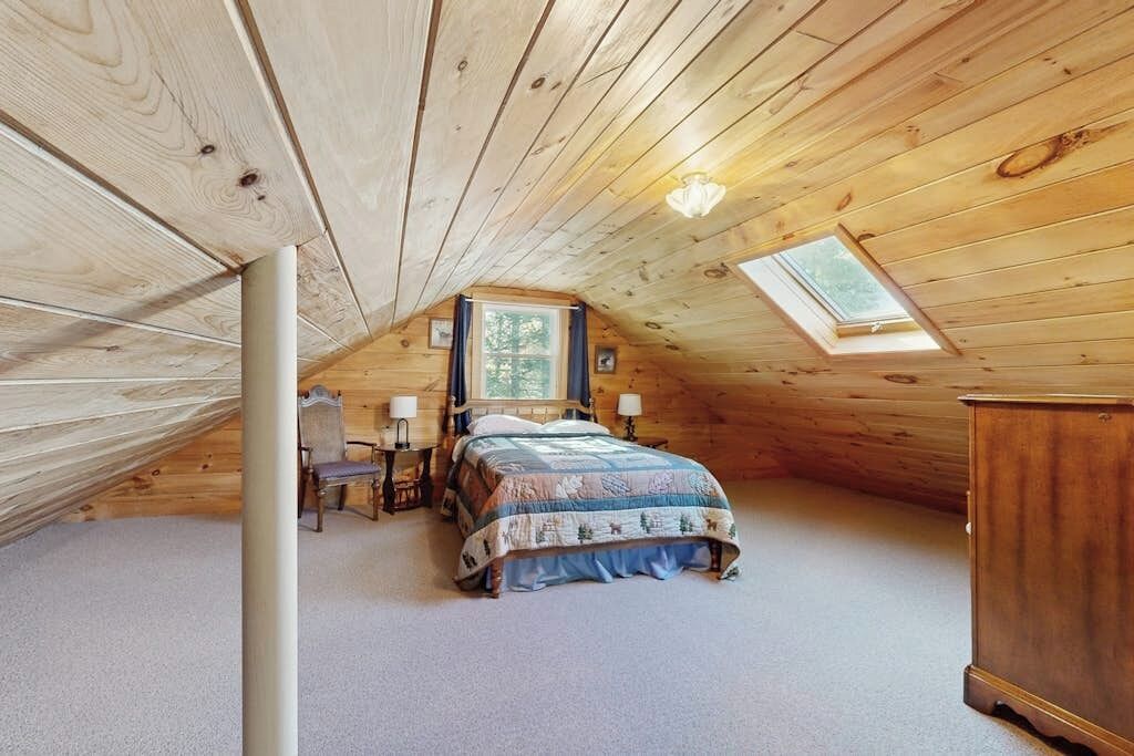 A cozy attic bedroom with a sloped ceiling, a bed, a desk, and a window.