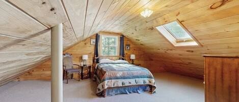 A cozy attic bedroom with a sloped ceiling, a bed, a desk, and a window.