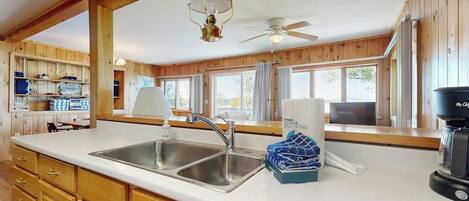 A kitchen with wooden cabinets, a double sink, a ceiling fan, and a coffee maker.