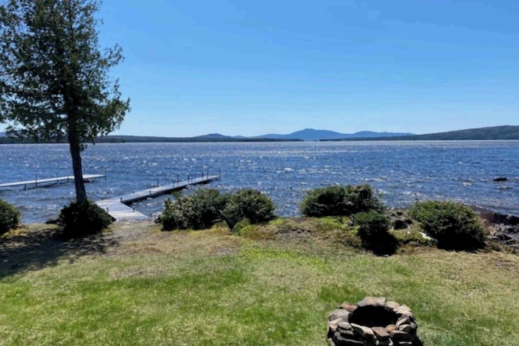 Vista sobre un lago con un muelle, zona de césped y una construcción de piedra.