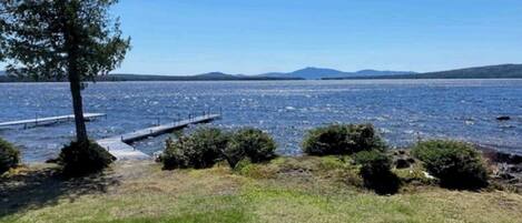 Vista sobre un lago con un muelle, zona de césped y una construcción de piedra.