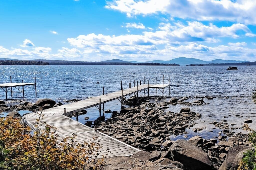 A rocky shoreline with wooden docks extending into calm water, surrounded by natural scenery.