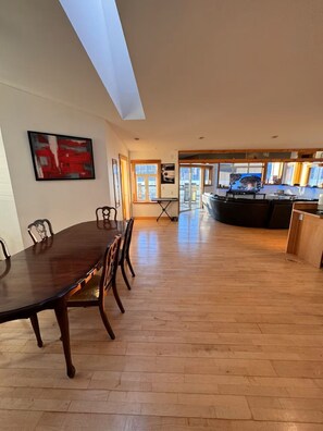 A spacious room with a long wooden dining table, chairs, a large abstract painting, and a kitchen area visible through an open doorway. - Lakeview Retreat | Wildlife & Serenity (Kelowna)