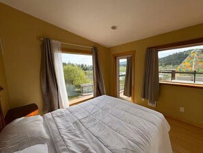 A bedroom with a large bed, two windows, and a view of a landscape. - Lakeview Retreat | Wildlife & Serenity (Kelowna)