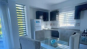 Une cuisine moderne avec une table à manger en verre, des meubles blancs et une vue sur l’extérieur.