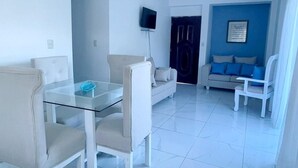 A modern living room with a glass dining table, two sofas, and a TV mounted on the wall. - A fully furnished, Beachside Apartment | Pool, Walk Everywhere (Calle Almirante)