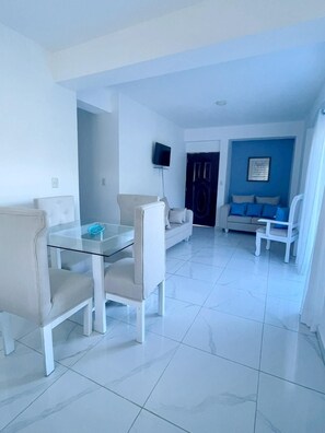 A modern living room with a glass dining table, two sofas, and a TV mounted on the wall. - A fully furnished, Beachside Apartment | Pool, Walk Everywhere (Calle Almirante)