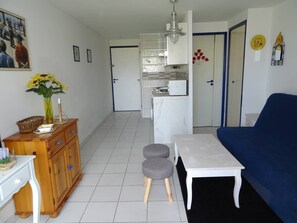 Ein Wohnzimmer mit einem blauen Sofa, einem weißen Tisch und einer Küchenzeile im Hintergrund.