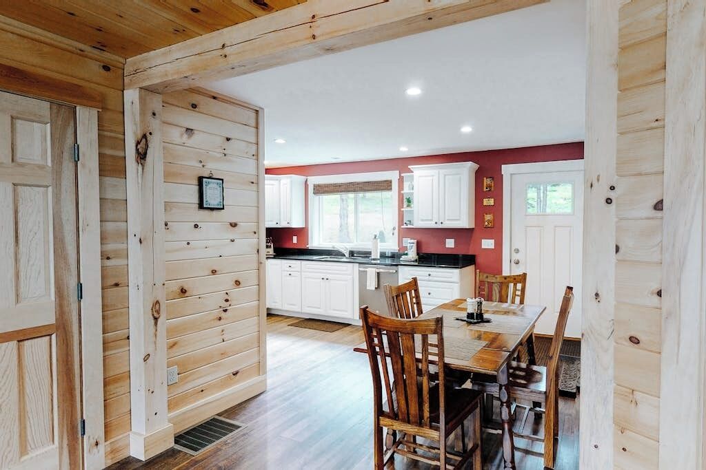 Un interior de madera con una mesa de comedor y sillas, armarios blancos y una pared de acento roja.