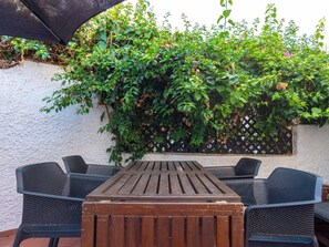 An outdoor patio with a wooden table and four chairs, surrounded by lush greenery and a white wall. - Apartment  by Interhome (Nerja)
