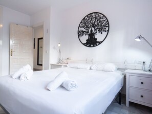 A hotel room with a large bed, two bedside tables, a wall-mounted lamp, and a door leading to another room. - Apartment  by Interhome (Nerja)