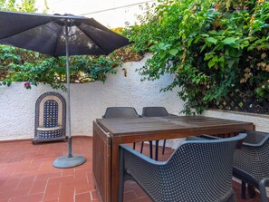 Eine Terrasse im Freien mit einem Holztisch und Stühlen, einem schwarzen Sonnenschirm und einer Wand mit Pflanzen.