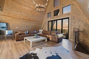 Ein moderner Loft-Raum mit Holzbalkendecke, einem Ecksofa, einem Couchtisch und einem großen Fenster mit Blick.