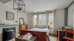 A bedroom with a wooden bed, a vintage trunk, a dresser, a desk, and a fireplace. - Sunrise on the Sheepscot- condo w/ deck overlooking the water - steps to dining & shopping (Wiscasset)