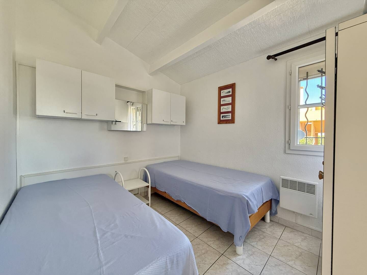 Een slaapkamer met twee eenpersoonsbedden, een klein bureau, een spiegel en een raam met uitzicht.