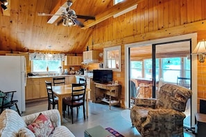 A wooden cabin interior with a dining area, kitchen, and a TV. - Lakefront, cabin-inspired home with firepit, grill, & screened porch, Wifi (Greenville)