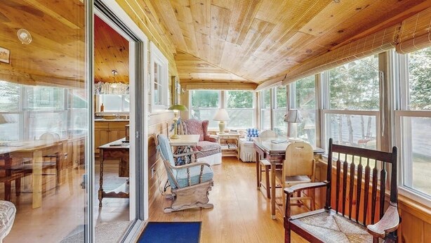 A wooden cabin interior with a dining area, seating, and large windows.