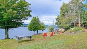 A lakeside view with a picnic table and chairs, surrounded by trees and a wooden structure.