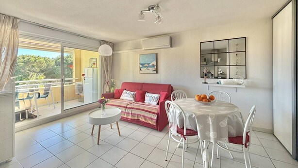 Un salon avec un canapé rouge, des fauteuils blancs, une petite table ronde et un balcon avec vue.