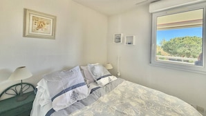 Une chambre à coucher comprenant un lit, une table de chevet, une lampe, un tableau encadré, une fenêtre avec vue et un thermostat.