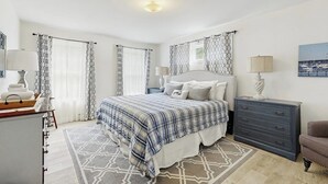 A bedroom with a bed, bedside tables, a dresser, a chair, and a painting on the wall.