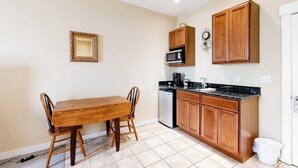A compact kitchen with a dining table, wooden cabinets, a microwave, and a sink. - Lovely downtown Northeast Harbor suite near the water and near Acadia (Northeast Harbor)
