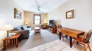 A living room with a sofa, a TV, a wooden dining table, and a ceiling fan. - Lovely downtown Northeast Harbor suite near the water and near Acadia (Northeast Harbor)