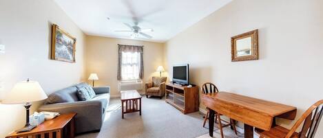 A living room with a sofa, a TV, a wooden dining table, and a ceiling fan.