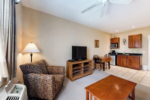 A living room with a sofa, TV, wooden entertainment unit, dining table, and kitchen area with cabinets and appliances.
