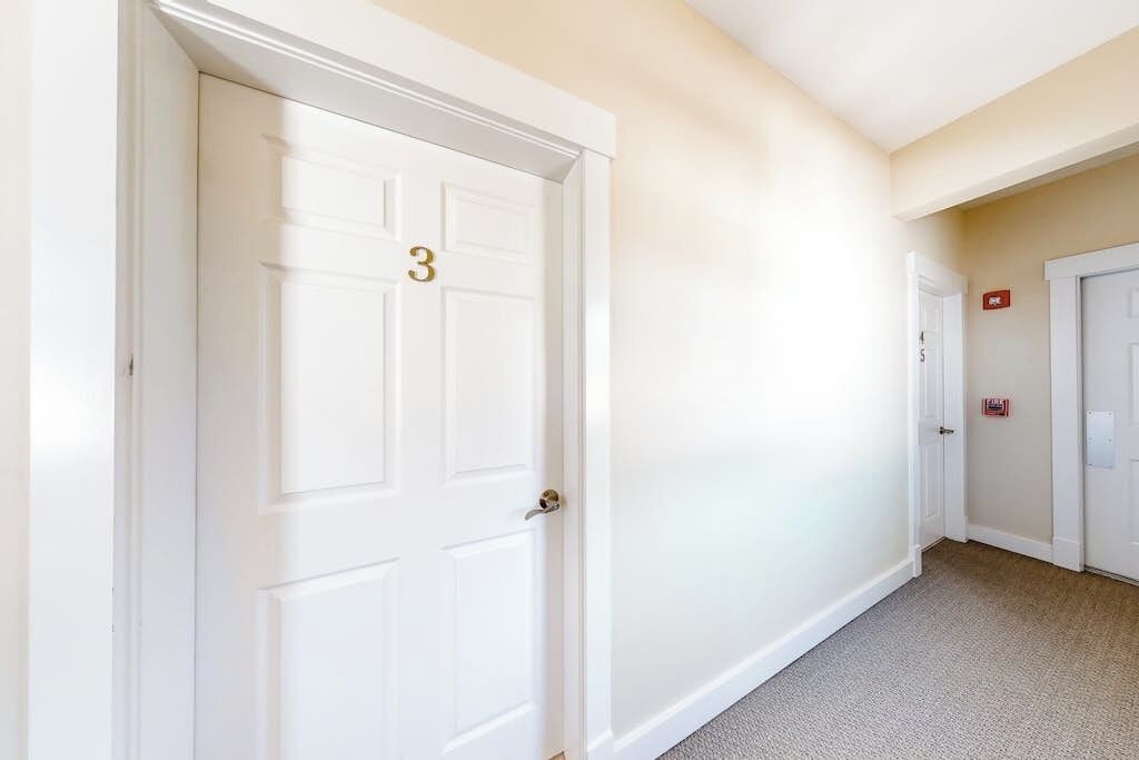 A hallway with white doors, one marked with the number 3, and a fire alarm on the wall.