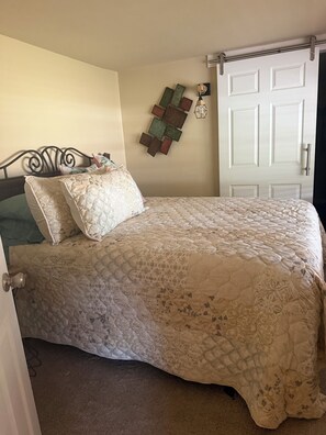 A bedroom with a bed, a door, and a wall-mounted light fixture. - Blue Sky Bungalow - 1-bedroom bungalow in Homosassa located just off 19! (Homosassa)