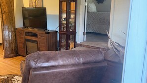 Ein Wohnzimmer mit einer Ledersofa, einem Fernseher, einem Holzschrank und einer Glastür zu einem anderen Raum.