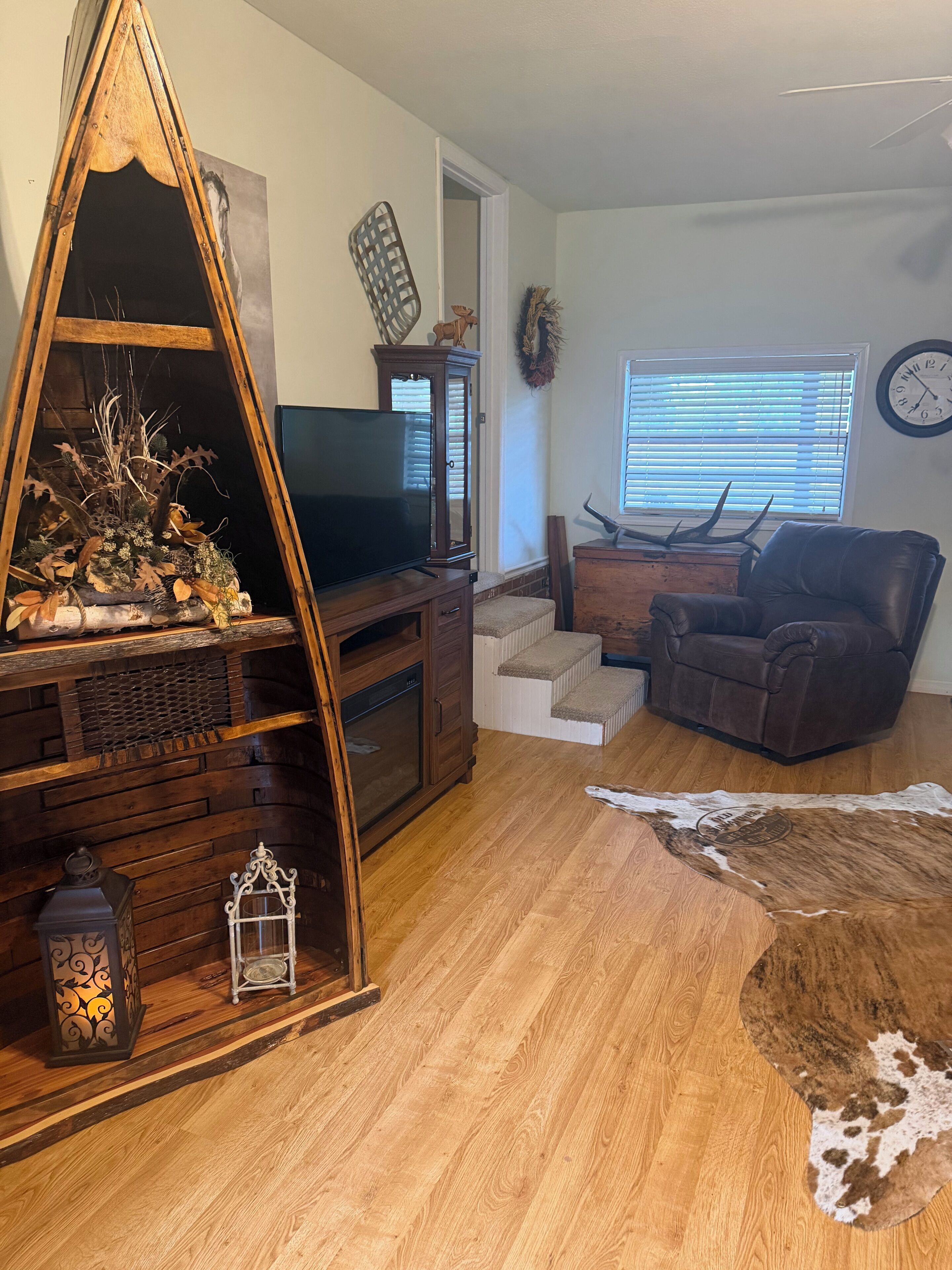 A living room with a wooden entertainment center, a television, a leather chair, and a cowhide rug.