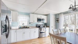 A modern kitchen with white cabinets, stainless steel appliances, and a wooden dining table. - Dog-friendly home with deck, pool table, & firepit - walk to downtown Boothbay (Boothbay Harbor)