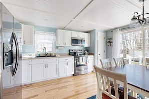 A modern kitchen with white cabinets, stainless steel appliances, and a wooden dining table.