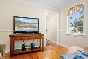 Een woonkamer met een flatscreen televisie op een houten standaard, een deur naar een andere kamer en een raam met gordijnen.