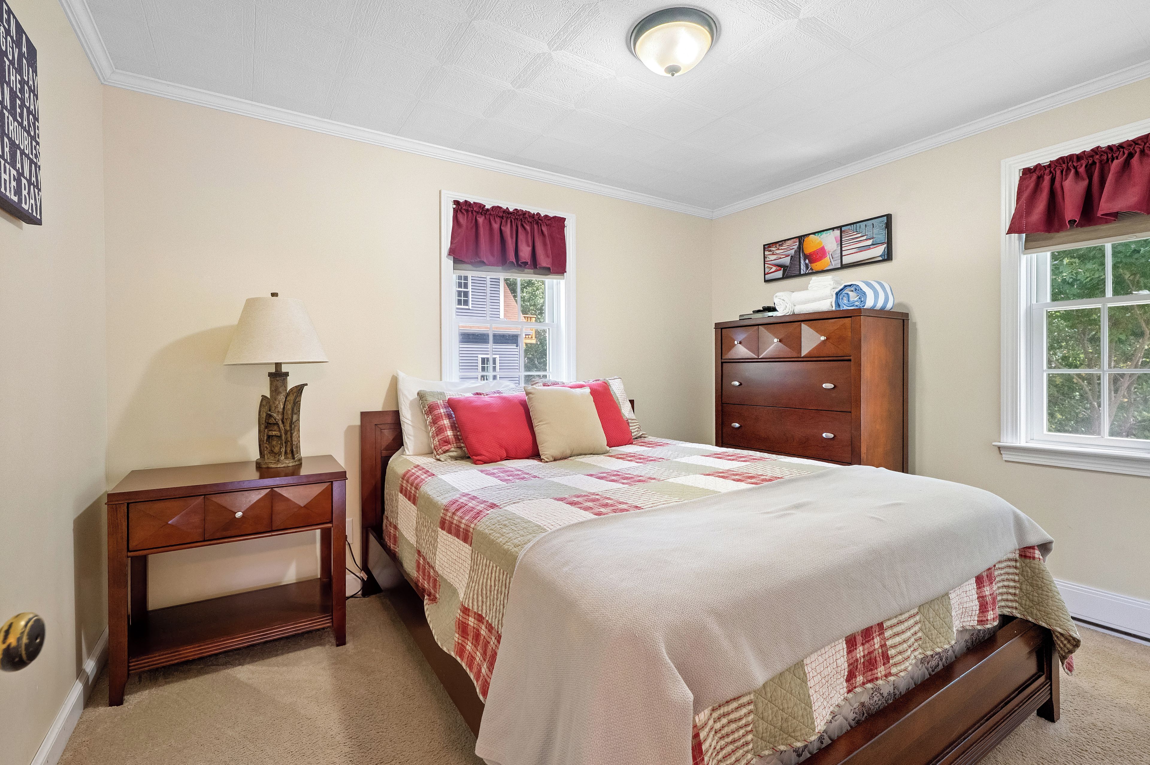 Un dormitorio con cama, mesita de noche, lámpara, cómoda y ventana con cortinas.