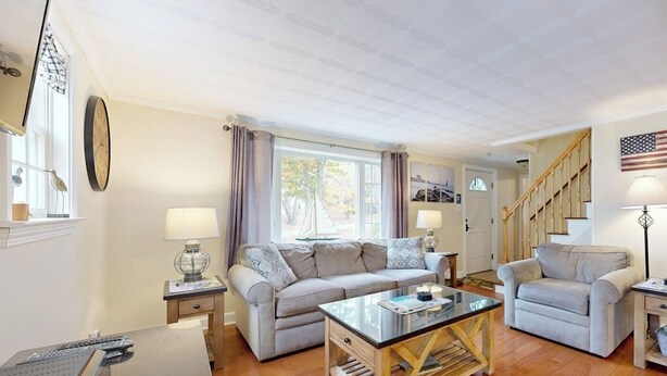 A living room with a sofa, armchairs, a coffee table, a lamp, a clock, and a staircase. - Boothbay Harbor Home with Water Views | Near Dining & Whale Watching (Boothbay Harbor)