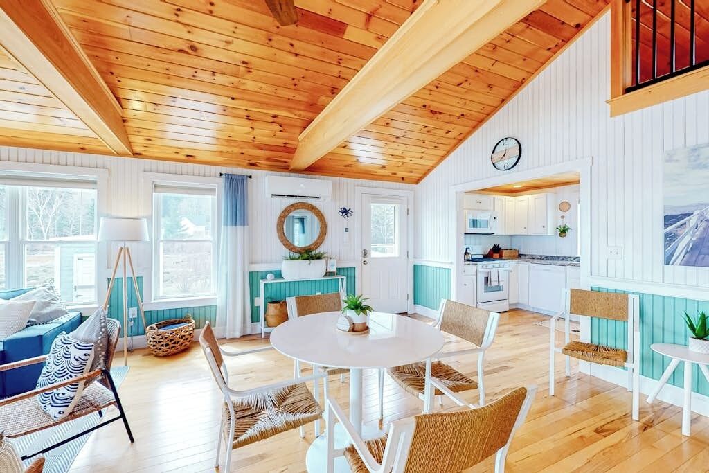 A cozy interior with a wooden ceiling, a dining area with a round table, and a kitchen with white cabinets.