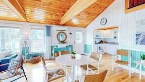 A cozy interior with a wooden ceiling, a dining area with a round table, and a kitchen with white cabinets.