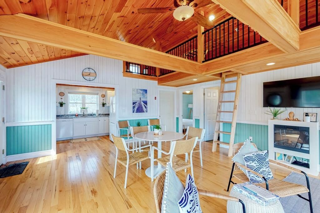 Une pièce spacieuse avec un plafond en bois, un coin repas avec des chaises, une cuisine avec des meubles blancs et un téléviseur.