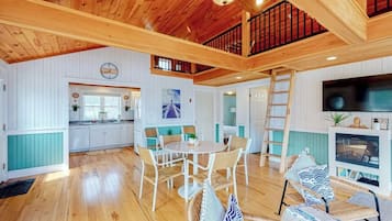 Une pièce spacieuse avec un plafond en bois, un coin repas avec des chaises, une cuisine avec des meubles blancs et un téléviseur.