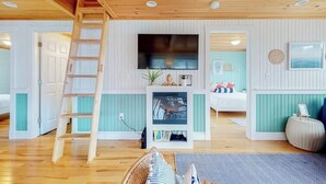 A room with a wooden ladder, a flat-screen TV, a small TV on a stand, a bed, a sofa, and a wall-mounted clock.