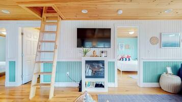 Une pièce avec une échelle en bois, un téléviseur à écran plat, un petit téléviseur posé sur un meuble, un lit, un canapé et une horloge fixée au mur.