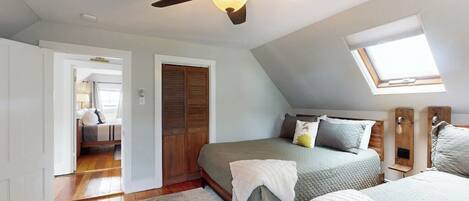 Een slaapkamer met twee bedden, een plafondventilator, een dakraam en uitzicht op een andere kamer.